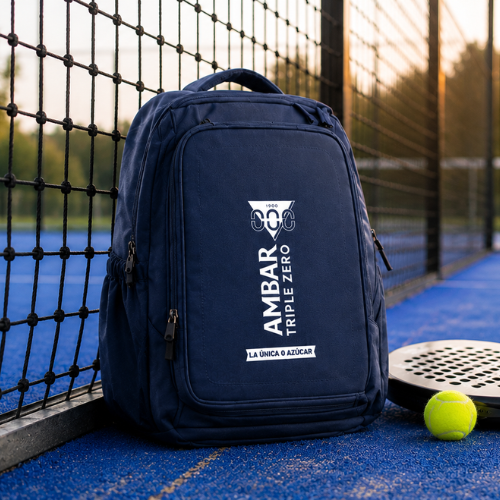 Mochila azul Ambar Triple Zero apoyada junto a pista de pádel con raqueta y pelota, con logotipo y lema “La única 0 azúcar” visibles