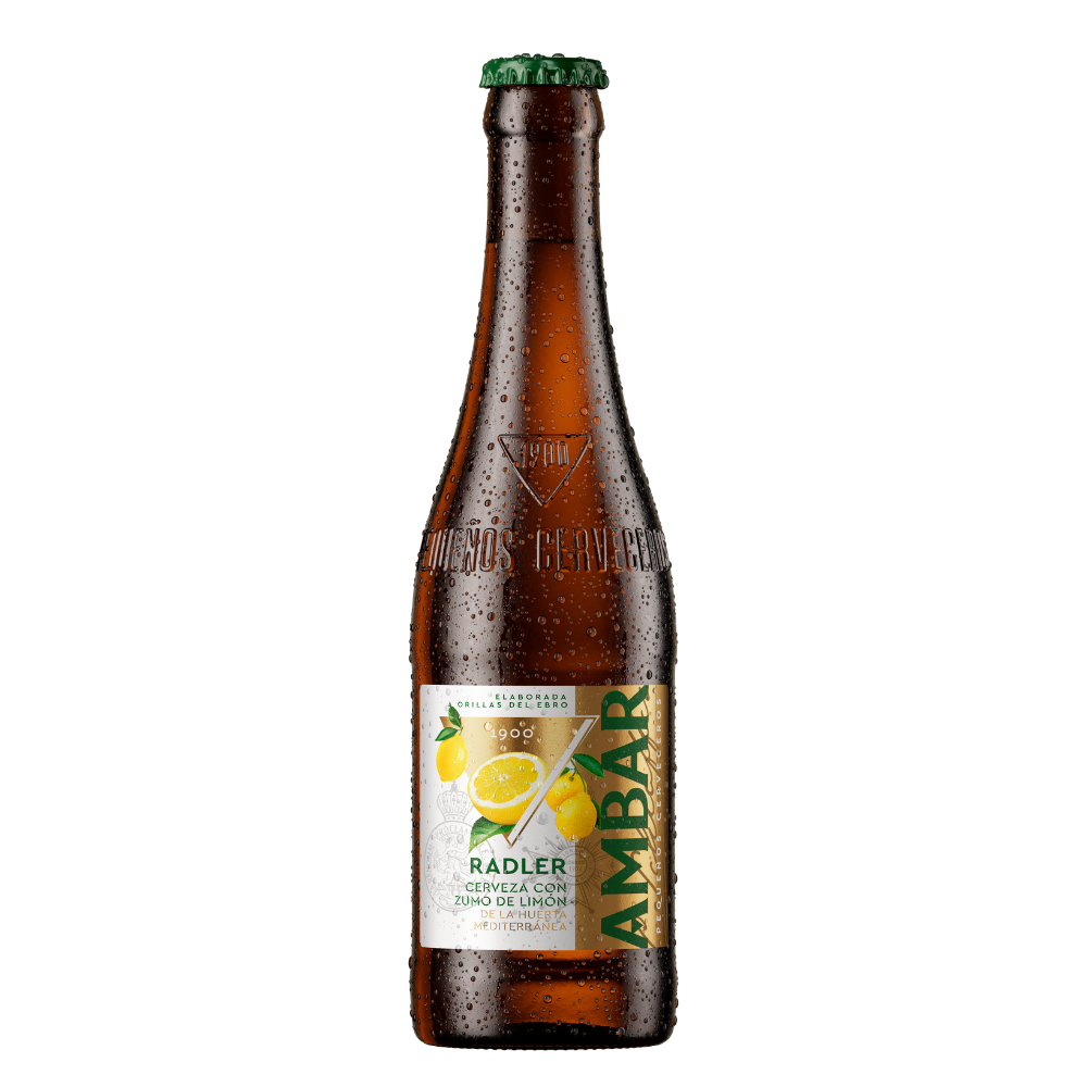 Botella de cerveza Ambar Radler fría cubierta de gotas de agua, con chapa verde y cristal marrón grabado en relieve con "1900" y "Pequeños Cerveceros". La etiqueta central combina blanco, dorado y verde, e incluye ilustraciones de limones frescos junto a la inscripción "RADLER - Cerveza con zumo de limón".